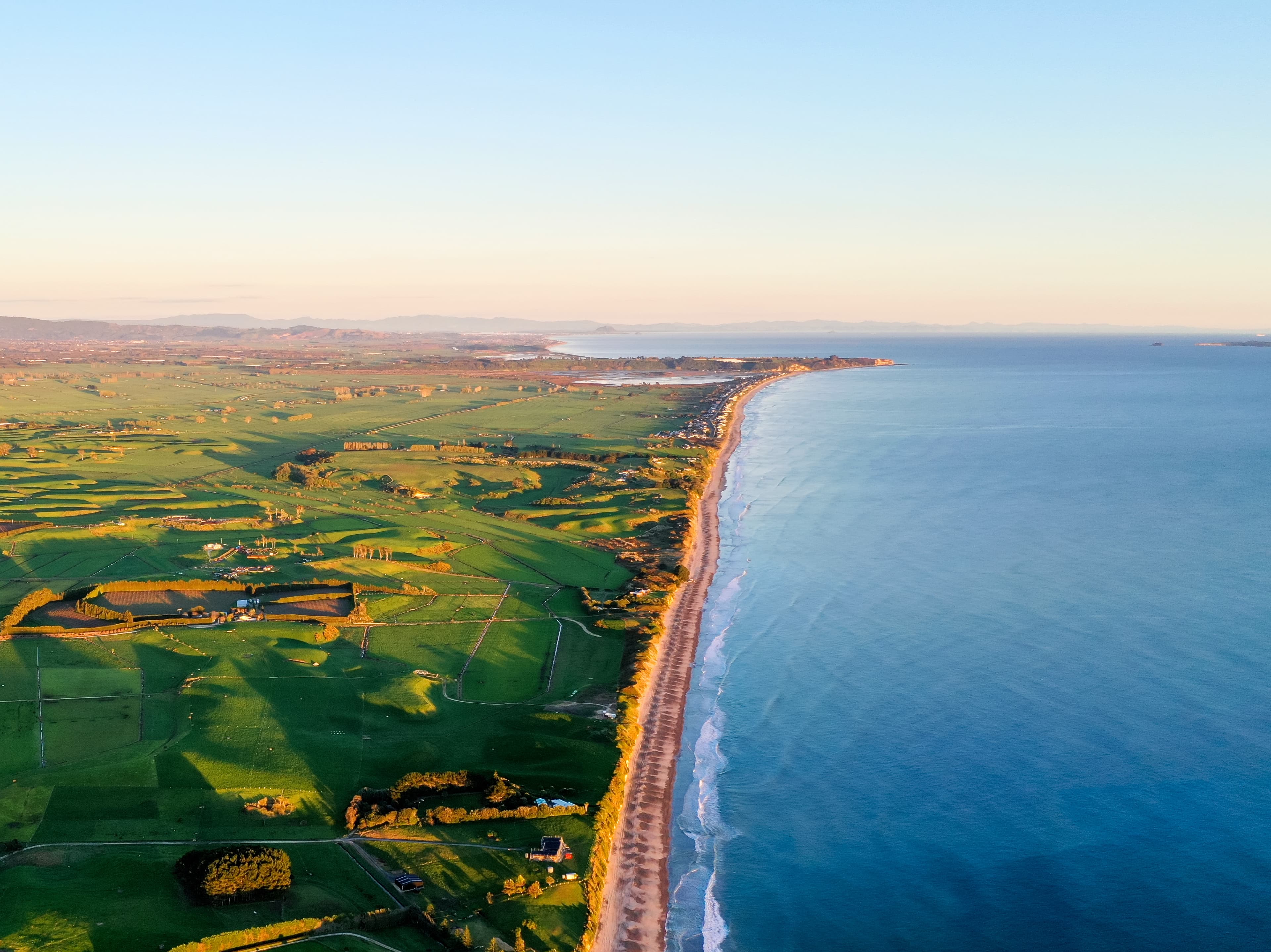 Aerial view of green farm paddocks meeting the coast in golden light